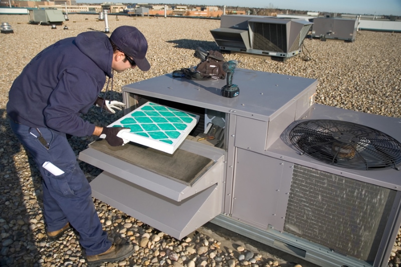 How to Reduce Your Company’s Energy Costs. Worker changing a roof top air exhange units filter.